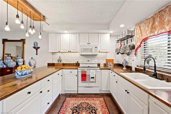 Kitchen with wood counters, white appliances, a textured ceiling, dark wood-style flooring, and recessed lighting | Image 14