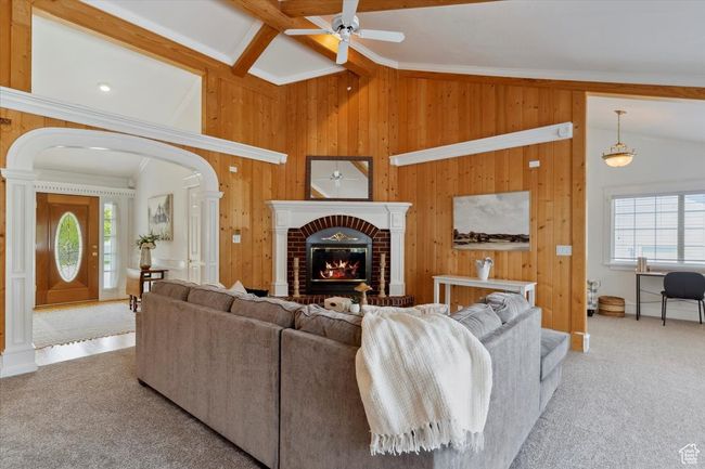 Living area featuring a ceiling fan, wooden walls, plenty of natural light, arched walkways, and carpet | Image 4