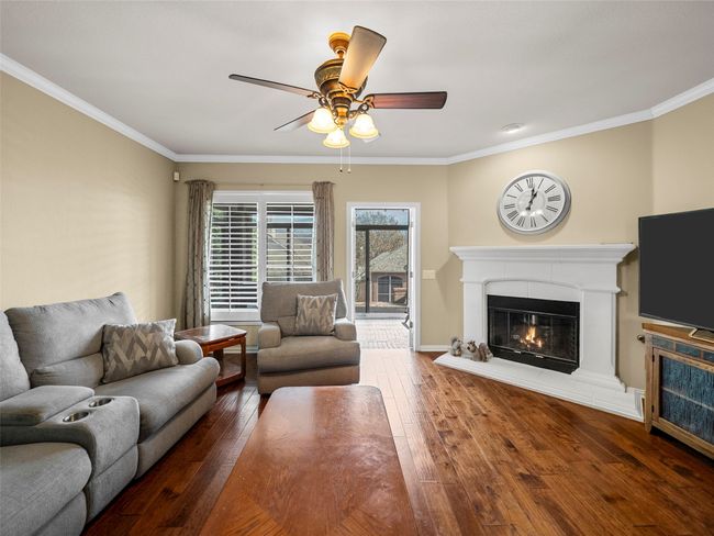 Living area featuring crown molding, hardwood / wood-style floors, a ceiling fan, a glass covered fireplace, and baseboards | Image 14