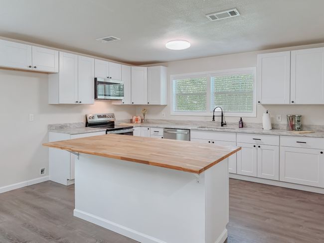 Kitchen featuring stainless steel appliances, wooden counters, light wood-style flooring, white cabinets, and a kitchen island | Image 14