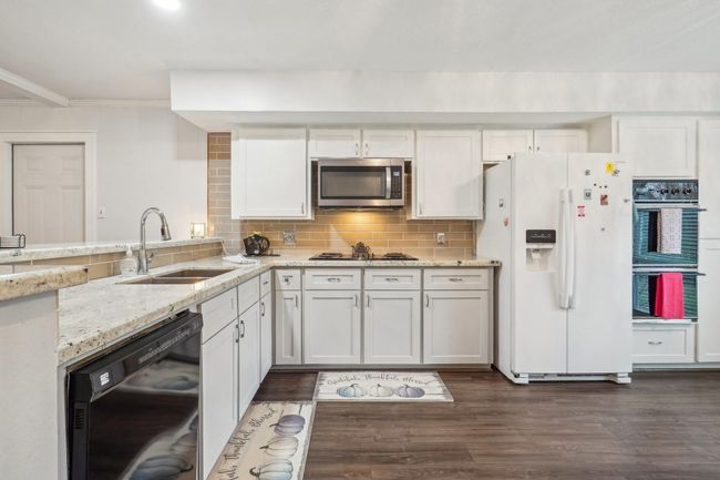 Spacious kitchen with natural light, featuring a dining area and a breakfast bar with granite countertops. The open layout connects to the living room. | Image 11