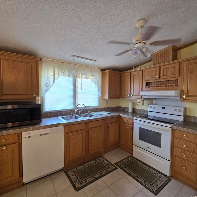 Kitchen with white appliances, vaulted ceiling, a ceiling fan, a textured ceiling, and ventilation hood | Image 16