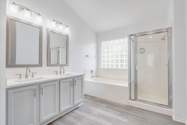 The spacious primary bathroom features his-and-hers walk-in closets, a new toilet, updated mirrors, luxury vinyl flooring, modern light fixtures, and a new quartz vanity countertop with dual sinks. It also includes a soaking tub and a separate walk-in shower for added comfort and convenience. | Image 14