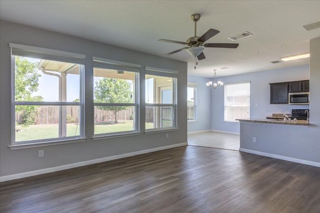 Spacious living room with a, ceiling fan, rich wood-look laminate flooring and crisp white baseboards—ready for your personal touch. | Image 5