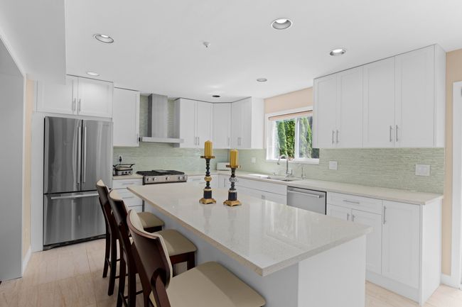 Kitchen with appliances with stainless steel finishes, wall chimney range hood, a breakfast bar area, white cabinetry, and recessed lighting | Image 9