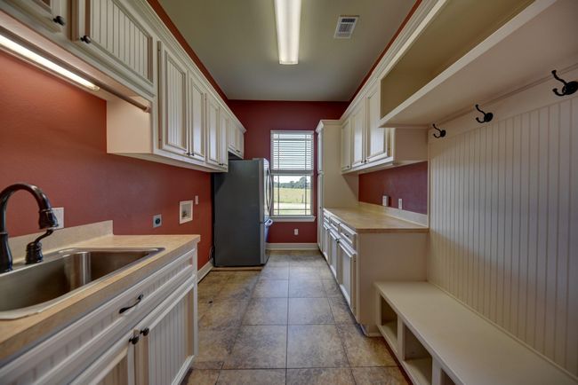 Spacious laundry and mudroom with abundant cabinetry, built-in bench with shelves, hooks, utility sink, and window views—designed for function and style. | Image 27