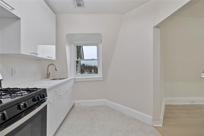 Kitchen with range with gas stovetop, baseboards, white cabinetry, visible vents, and a sink | Image 12