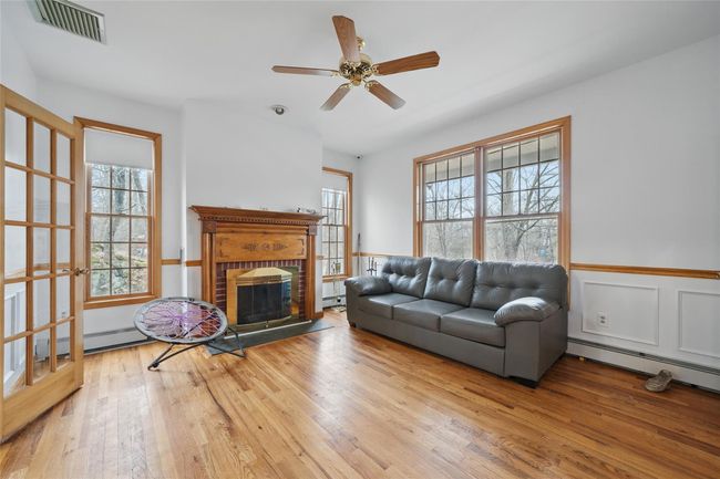 Living room with baseboard heating, a baseboard radiator, a ceiling fan, wood finished floors, and visible vents | Image 23