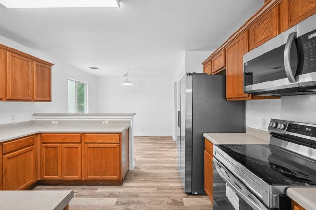 Kitchen with appliances with stainless steel finishes, brown cabinets, light countertops, a peninsula, and light wood-style flooring | Image 16