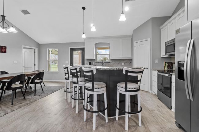 Kitchen with visible vents, appliances with stainless steel finishes, a breakfast bar area, vaulted ceiling, and backsplash | Image 6