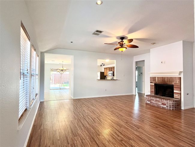 Unfurnished living room featuring wood finished floors, a chandelier, a ceiling fan, a fireplace, and vaulted ceiling | Image 8