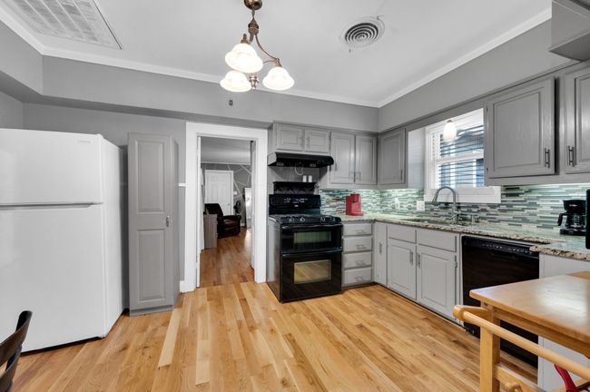 Kitchen featuring black appliances, under cabinet range hood, gray cabinetry, a sink, and crown molding | Image 8