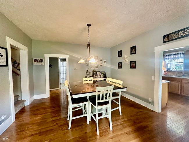 dining space with dark wood finished floors, healthy amount of natural light, a textured ceiling, a chandelier, and stairway | Image 18