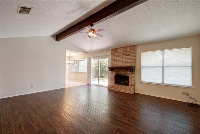 Unfurnished living room with baseboards, ceiling fan, vaulted ceiling with beams, gas fireplace. | Image 9