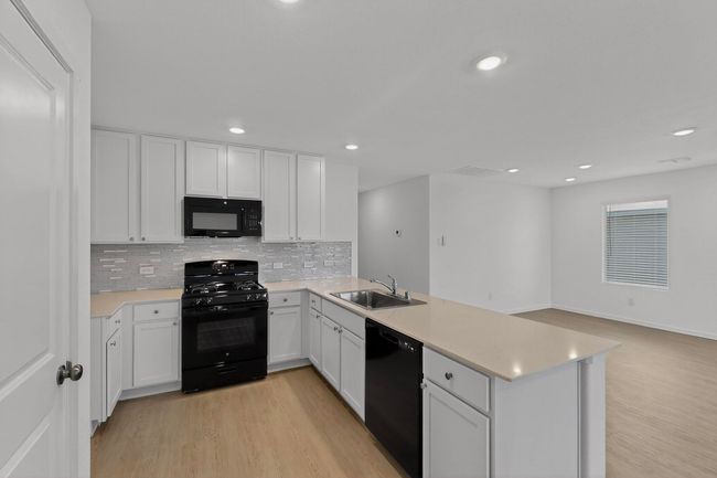 Kitchen featuring black appliances, a peninsula, a sink, backsplash, and light countertops | Image 10