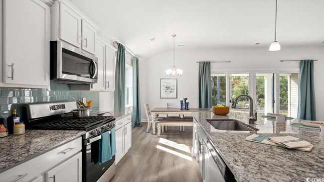 Kitchen with stainless steel appliances, a sink, light wood finished floors, decorative backsplash, and a chandelier | Image 5