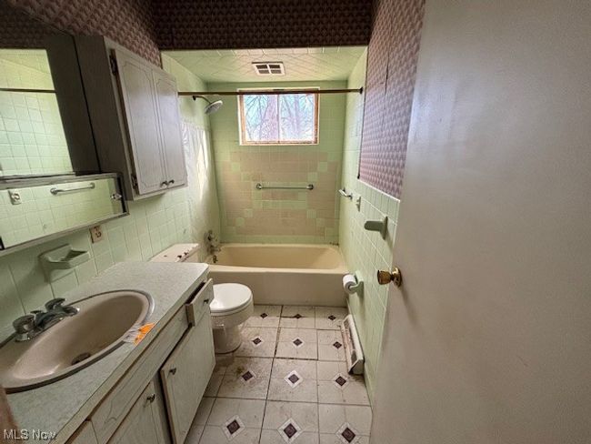 Full bathroom featuring vanity with extensive cabinet space, tiled shower / bath, tile walls, toilet, and tile flooring | Image 12