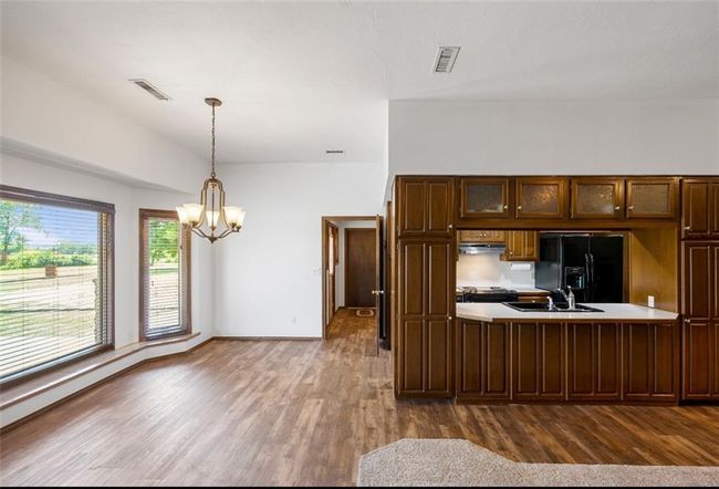 Kitchen with visible vents, black fridge with ice dispenser, dark wood finished floors, and a sink | Image 9