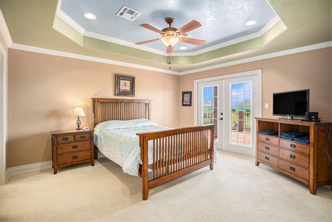 This spacious primary bedroom boasts a sophisticated tray ceiling and two sets of elegant French doors that open to the outside deck. The room is well-illuminated by a ceiling fan and recessed lighting, and is further enhanced by the refined touch of crown molding. | Image 16