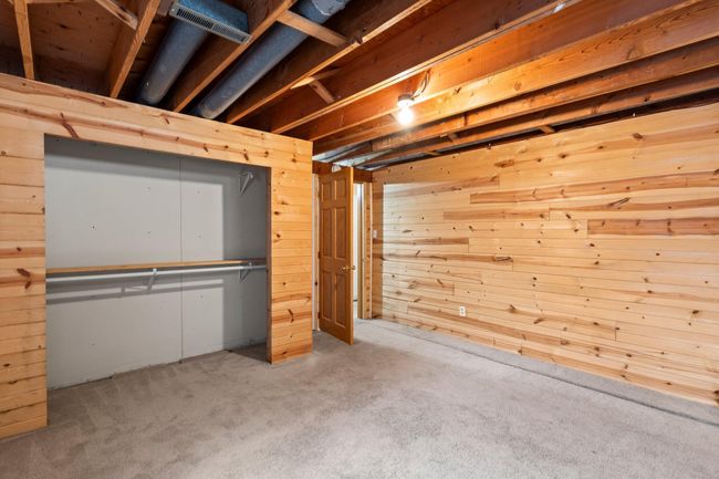 The home's third bedroom, located in the basement, features carpeting, wood-paneled walls, and a spacious closet. | Image 14