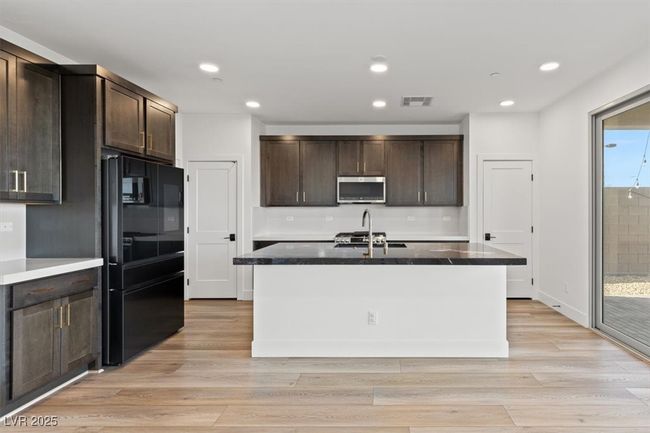 Kitchen featuring stainless steel microwave, freestanding refrigerator, dark brown cabinets, a sink, and visible vents | Image 27