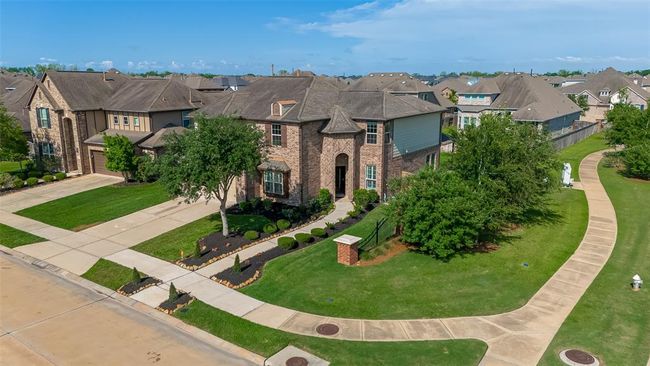 Two-story brick home with a well-maintained lawn and landscaping. It features a wide driveway and is situated in a neighborhood with similar homes, offering a suburban feel with nearby sidewalks and greenery. | Image 42