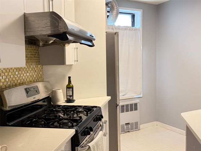 Kitchen with appliances with stainless steel finishes, under cabinet range hood, radiator, light countertops, and tasteful backsplash | Image 5
