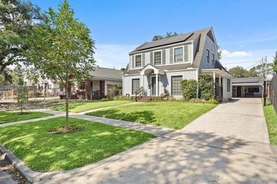 Charming two-story home featuring a gray exterior with white trim and a quaint front porch. The house is equipped with solar panels and flanked by mature landscaping, offering both curb appeal and energy efficiency. | Image 1