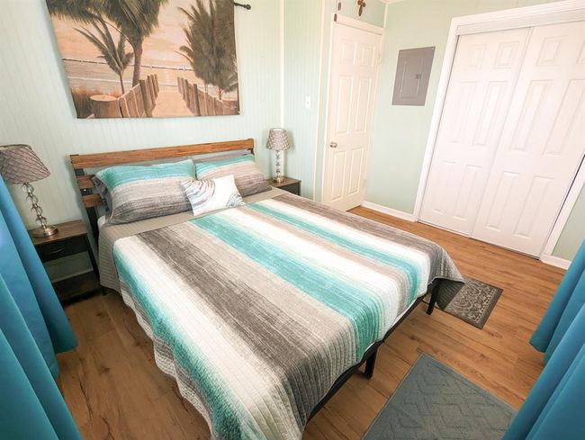 This bedroom features a beach-themed decor with a queen-sized bed, and ample closet space. Light pastel walls and a large beach painting create a relaxing atmosphere. | Image 14