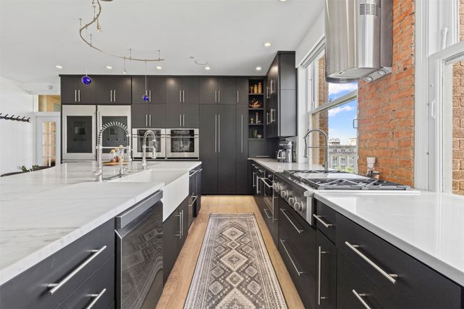 Kitchen featuring wall chimney exhaust hood, light wood finished floors, wine cooler, dark cabinets, and appliances with stainless steel finishes | Image 8