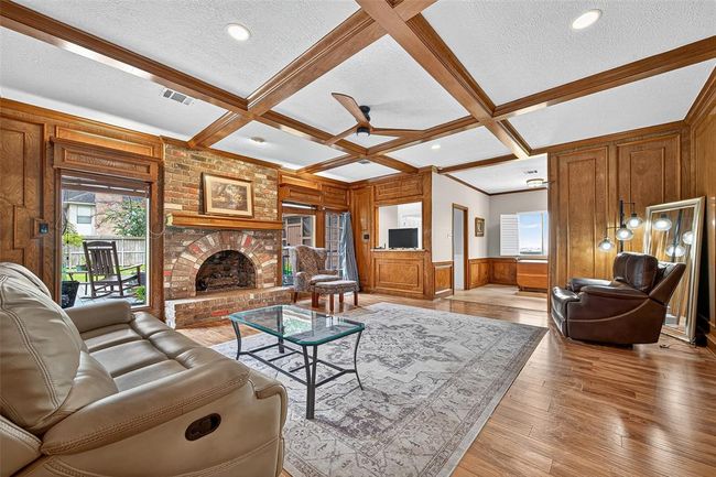 A cozy yet expansive retreat with wood-paneled walls, a coffered ceiling, and a brick fireplace that feels like it belongs in a storybook. Picture windows invite in daylight, while details evoke a sense of comfort rooted in tradition. | Image 14