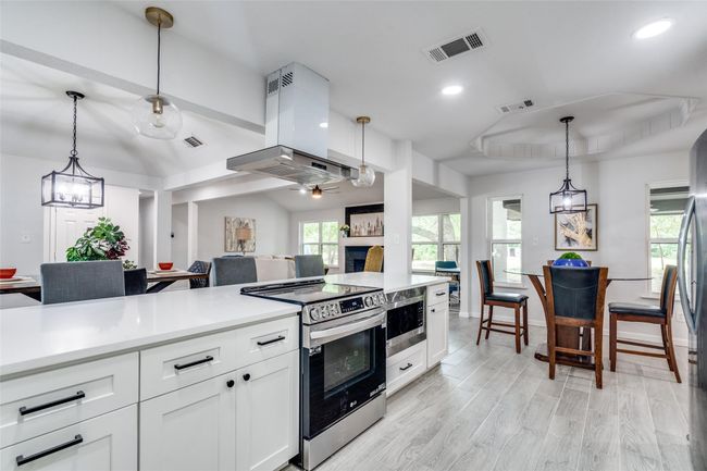 Kitchen featuring hanging light fixtures, white cabinetry, appliances with stainless steel finishes, island range hood, and open floor plan | Image 7