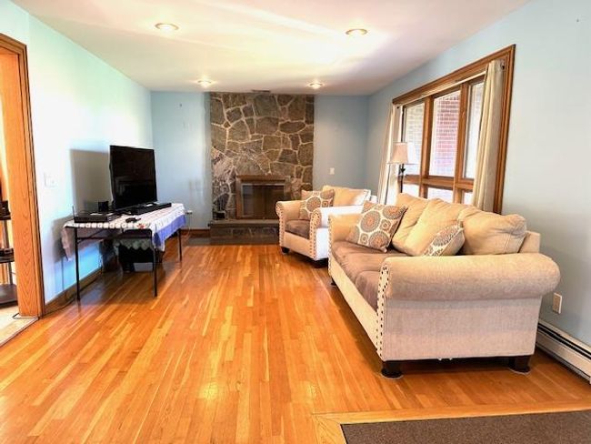 Living room with a stone fireplace, wood-type flooring, and baseboard heating | Image 6