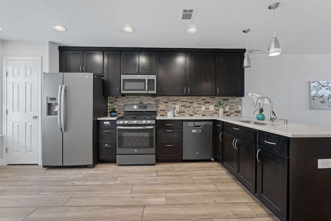 Kitchen featuring stainless steel appliances, wood tiled floors, decorative backsplash, light countertops, and recessed lighting | Image 5