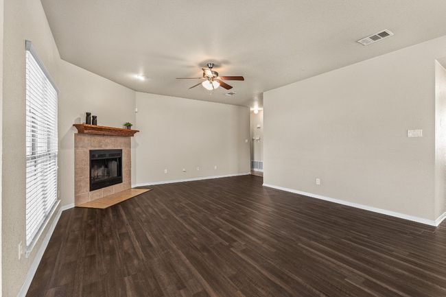 Unfurnished living room with a ceiling fan, a tile fireplace, and dark wood-style flooring | Image 17
