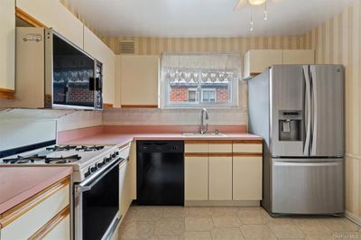 Kitchen featuring cream cabinetry, black dishwasher, stainless steel fridge, white gas stove, and sink | Image 3