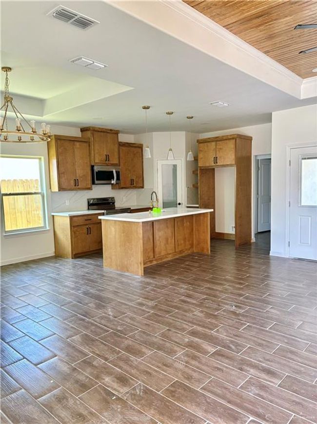 Kitchen featuring visible vents, stainless steel appliances, a tray ceiling, brown cabinetry, and a notable chandelier | Image 8