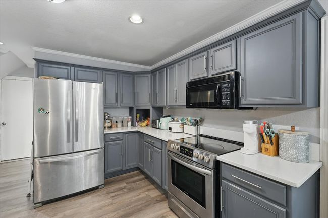 Kitchen featuring stainless steel appliances, gray cabinets, light wood-type flooring, light countertops, and ornamental molding | Image 13
