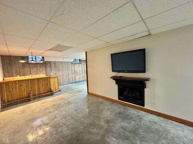 indoor bar featuring baseboards, a drop ceiling, wooden walls, a fireplace, and concrete flooring | Image 62