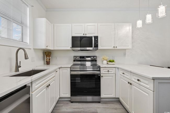 Kitchen with appliances with stainless steel finishes, ornamental molding, white cabinetry, a peninsula, and light wood finished floors | Image 9