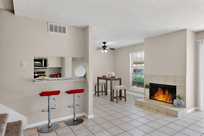 Kitchen featuring appliances with stainless steel finishes, a kitchen bar, a tiled fireplace, a ceiling fan, and a textured ceiling | Image 15