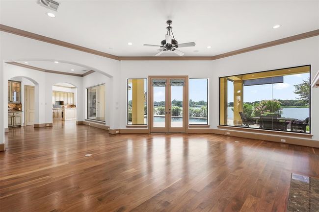 This spacious living area features elegant Brazilian Walnut hardwood floors, large windows with stunning lake views, and a view of the covered outdoor patio. The open layout flows seamlessly into the dining room and kitchen, perfect for entertaining and enjoying natural light. | Image 12