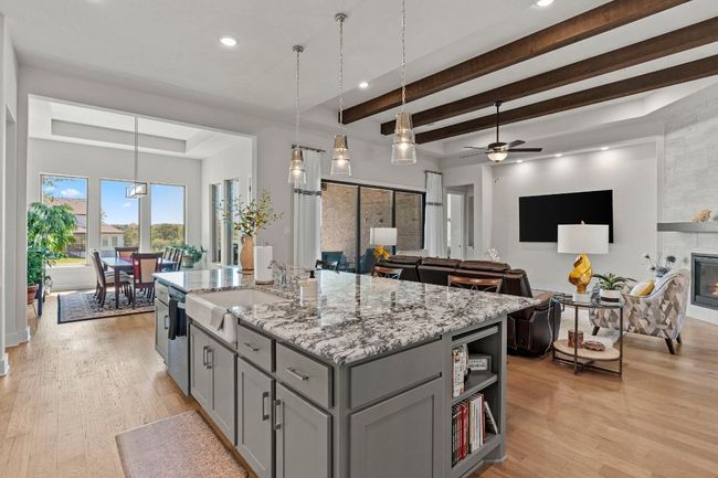 Kitchen with a center island with sink, light stone counters, a sink, and decorative light fixtures | Image 18