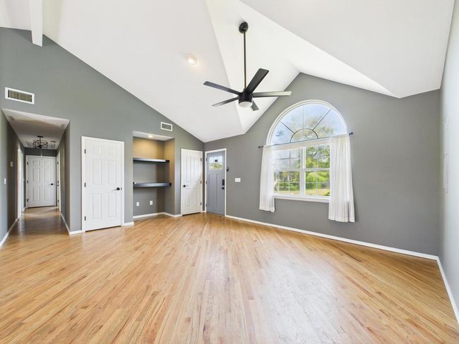 Unfurnished living room featuring built in features, a ceiling fan, light wood-style floors, high vaulted ceiling, and beam ceiling | Image 12