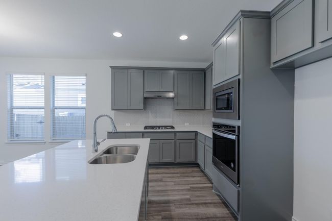 Kitchen with stainless steel appliances, under cabinet range hood, a sink, light countertops, and gray cabinets | Image 15