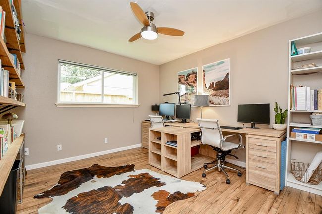 This home office features a spacious layout with a large window for natural light, wooden floors, and ample shelving. It includes a stylish ceiling fan and a dual desk setup, ideal for productivity. | Image 33