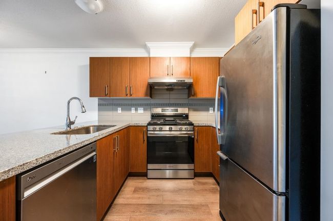 Kitchen with appliances with stainless steel finishes, under cabinet range hood, brown cabinets, light wood-type flooring, and ornamental molding | Image 4