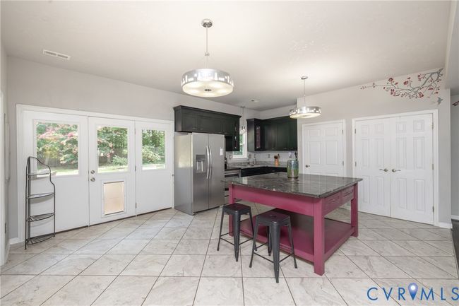 Kitchen with stainless steel fridge, hanging light fixtures, dark stone countertops, open shelves, and a kitchen bar | Image 35