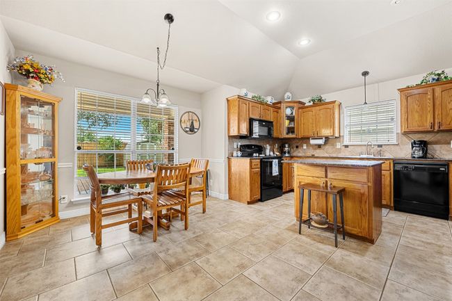 Kitchen with black appliances, backsplash, lofted ceiling, glass insert cabinets, and a center island | Image 10