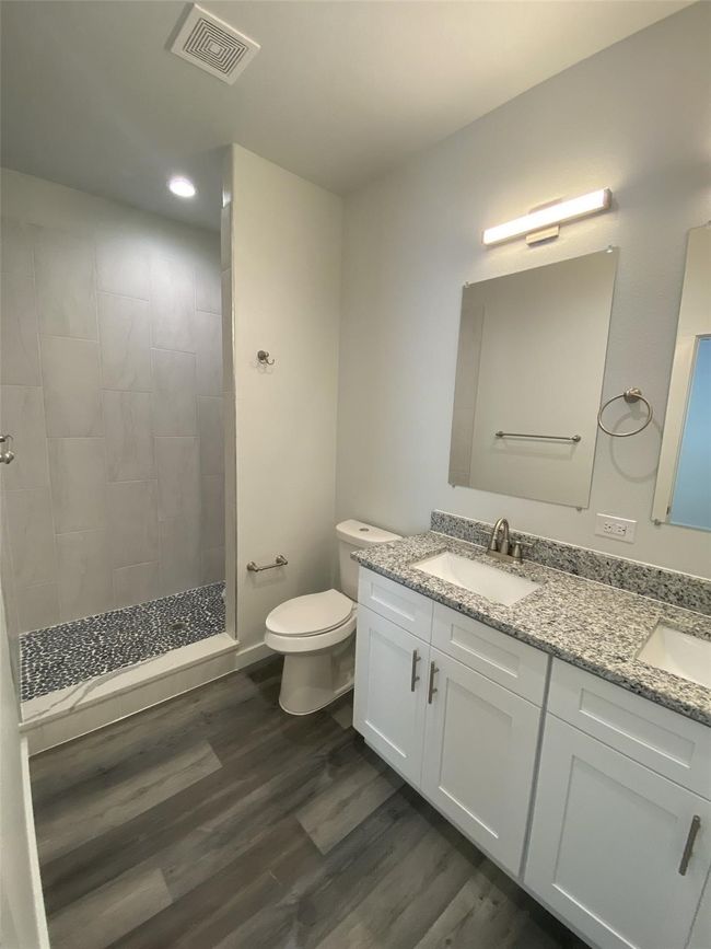 Bathroom featuring double vanity, toilet, wood finished floors, a tile shower, and recessed lighting | Image 11